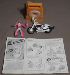 The paperwork, wind up base, motorcycle & doll with jumpsuit and 